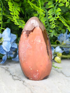 a large, colorful rock formation with a unique, textured surface, surrounded by lush greenery and blue flowers.