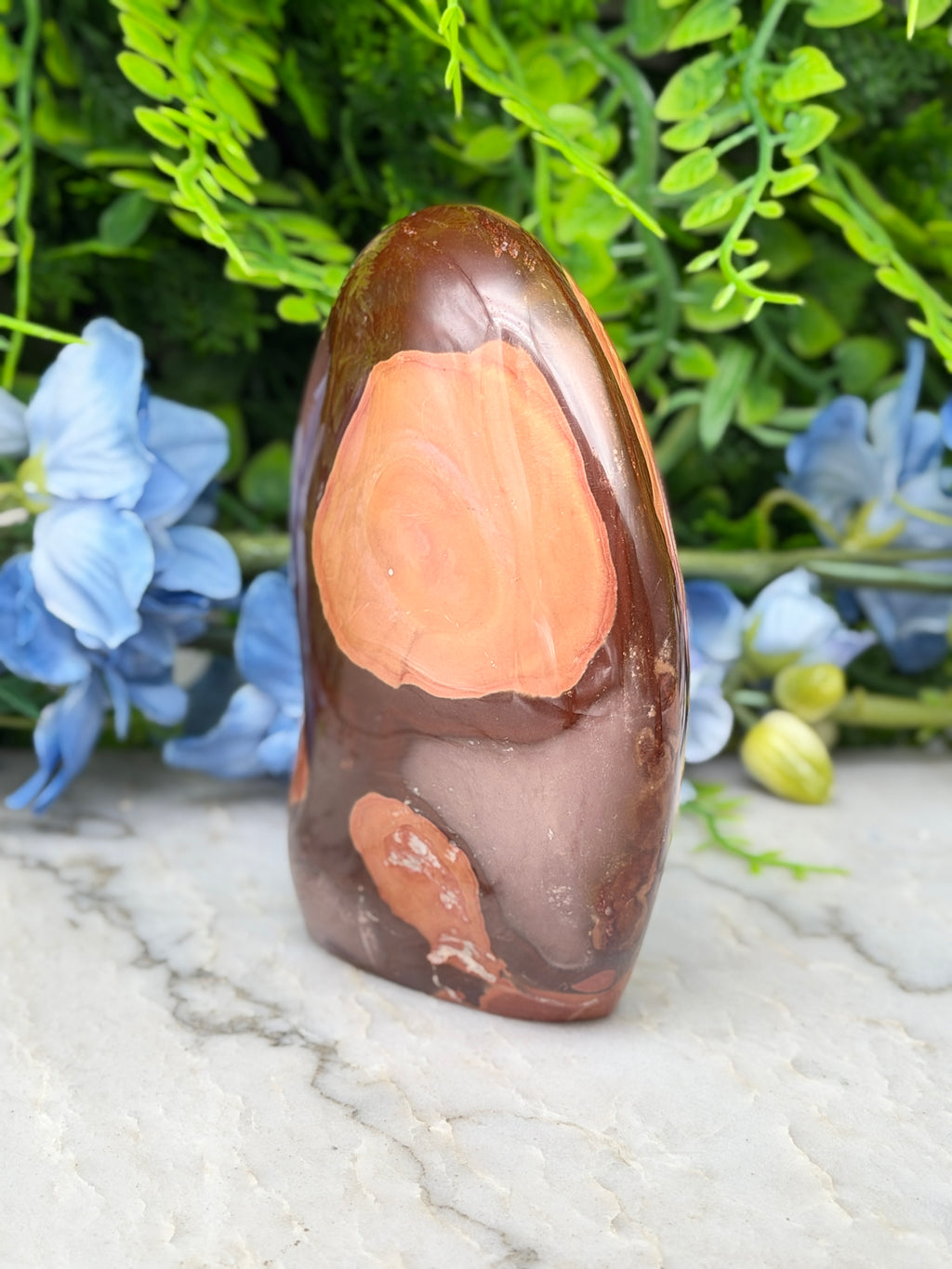 a brown and orange rock with a unique pattern, placed on a white surface surrounded by blue flowers.