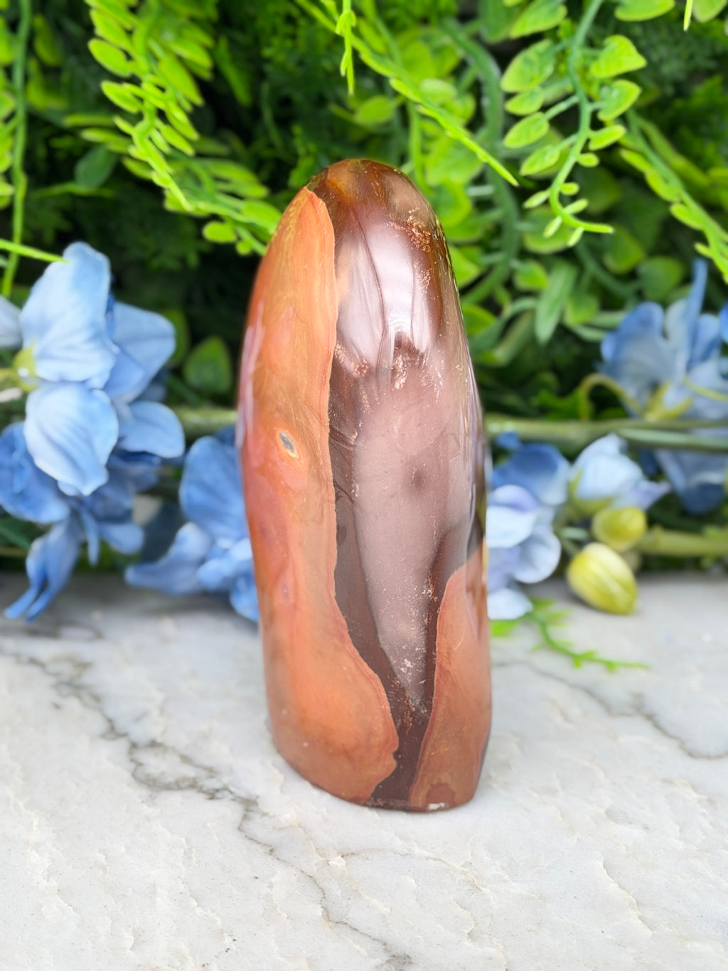 a brown, jagged rock with a unique, irregular shape, surrounded by blue flowers and green foliage.