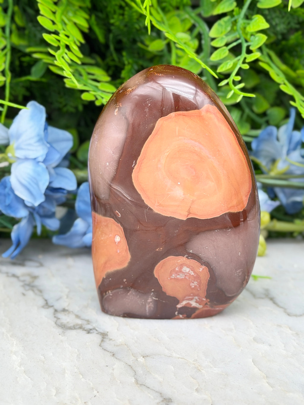 A jadeite, a type of jadeite, is displayed on a marble surface, surrounded by blue flowers.