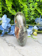 a large, dark green rock with a brownish hue, placed on a white surface. The rock is surrounded by a variety of blue and green flowers, creating a visually appealing contrast.