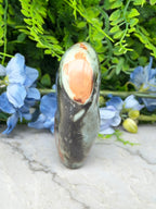 a unique, colorful rock formation with a hole in the center, surrounded by lush green foliage and blue flowers.