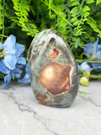 a large, colorful rock with a unique pattern, placed on a marble surface surrounded by blue flowers.