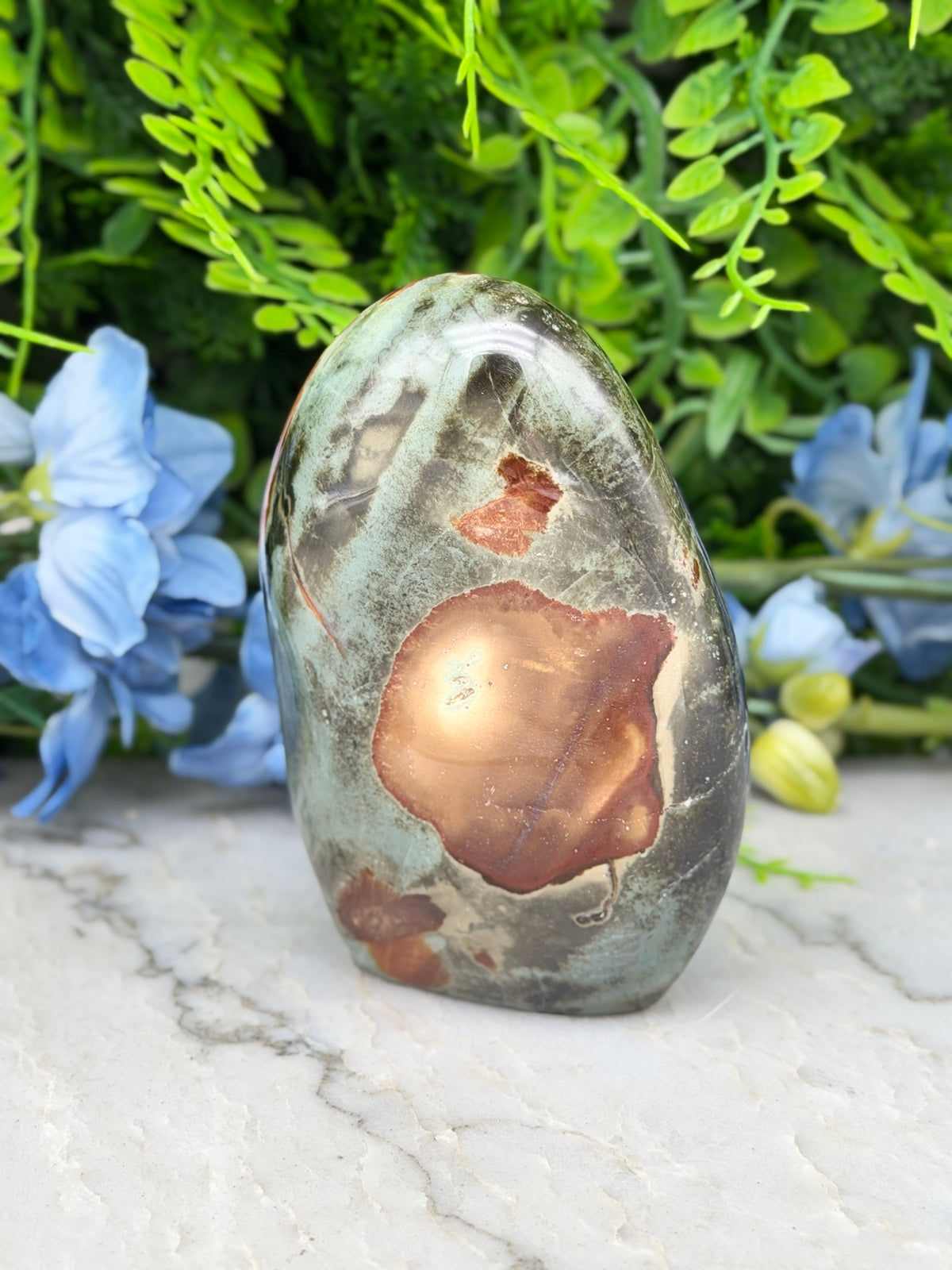 a large, colorful rock with a unique pattern, placed on a marble surface surrounded by blue flowers.