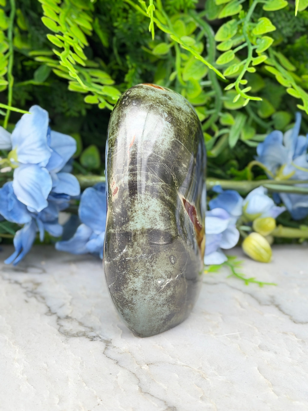 a large, dark green, and possibly black stone or gemstone, surrounded by a variety of blue flowers and green foliage.