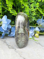 a large, dark green, and possibly black stone or gemstone, surrounded by a variety of blue flowers and green foliage.