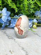a white and brown rock with a unique pattern, placed on a marble surface. The rock is surrounded by blue flowers, creating a visually appealing contrast.