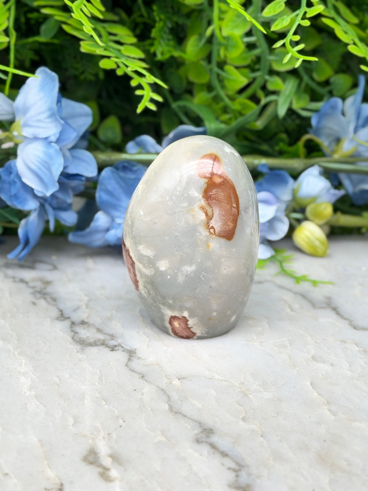 a gray rock with brown spots, placed on a marble surface, surrounded by blue flowers.