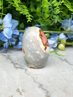 a white and brown speckled rock sitting on a marble surface, surrounded by blue flowers.