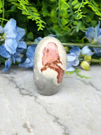 a white rock with a pinkish-brown pattern on it, placed on a marble surface. The rock is surrounded by blue flowers, creating a visually appealing contrast.