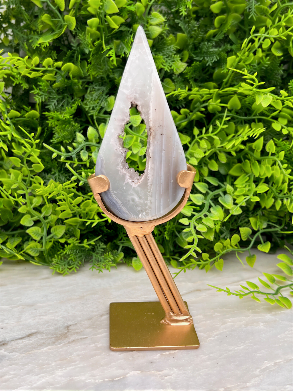 A white, triangular-shaped rock with a hole in the center, displayed on a gold stand in front of a lush, green plant.