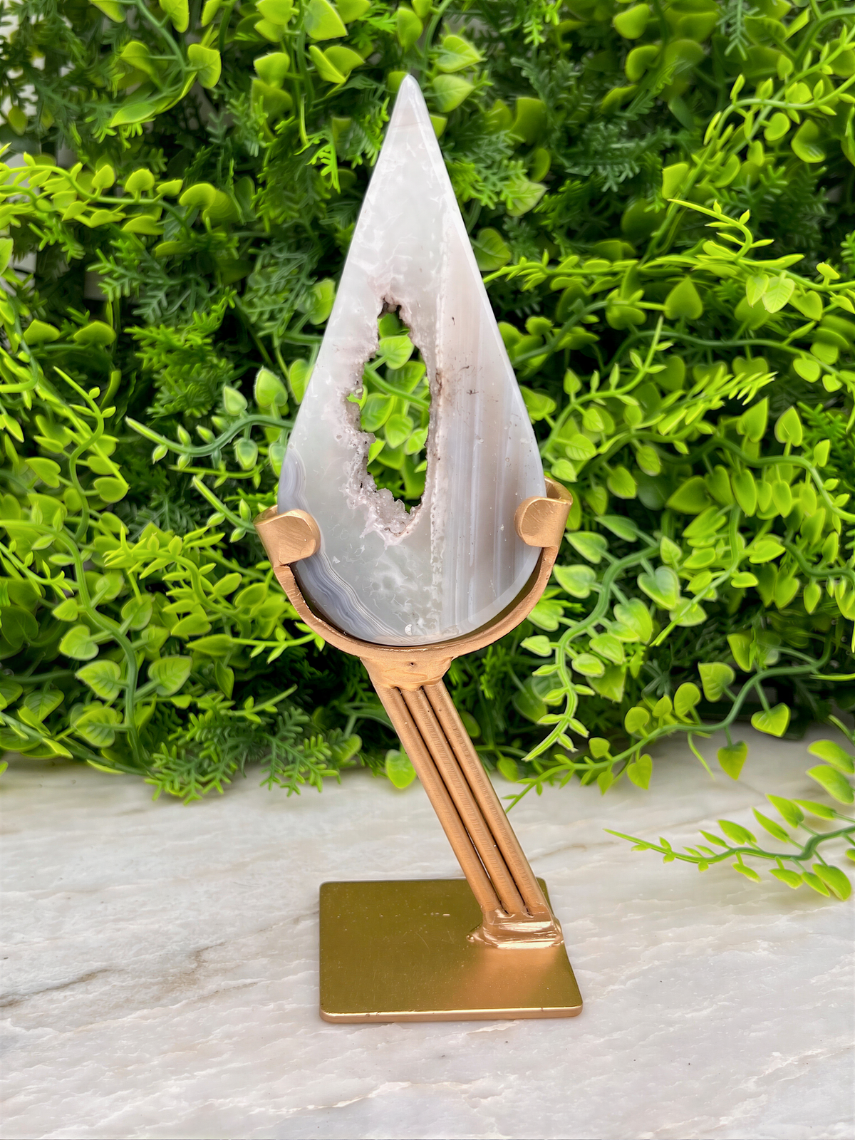 A white, triangular-shaped rock with a hole in the center, displayed on a gold stand in front of a lush, green plant.