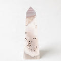 A tall, pointed crystal formation with a pinkish-white hue and scattered black dots on its surface.