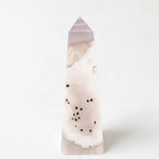 A tall, pointed crystal formation with a pinkish-white hue and scattered black dots on its surface.