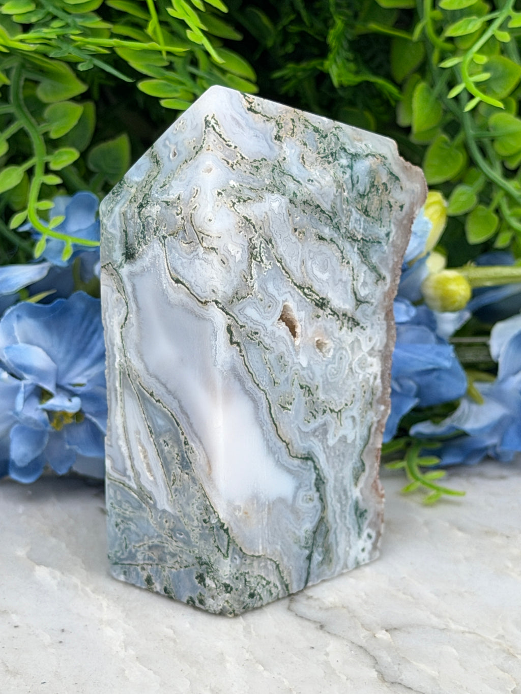 a close-up view of a jade crystal surrounded by lush green foliage and delicate blue flowers.