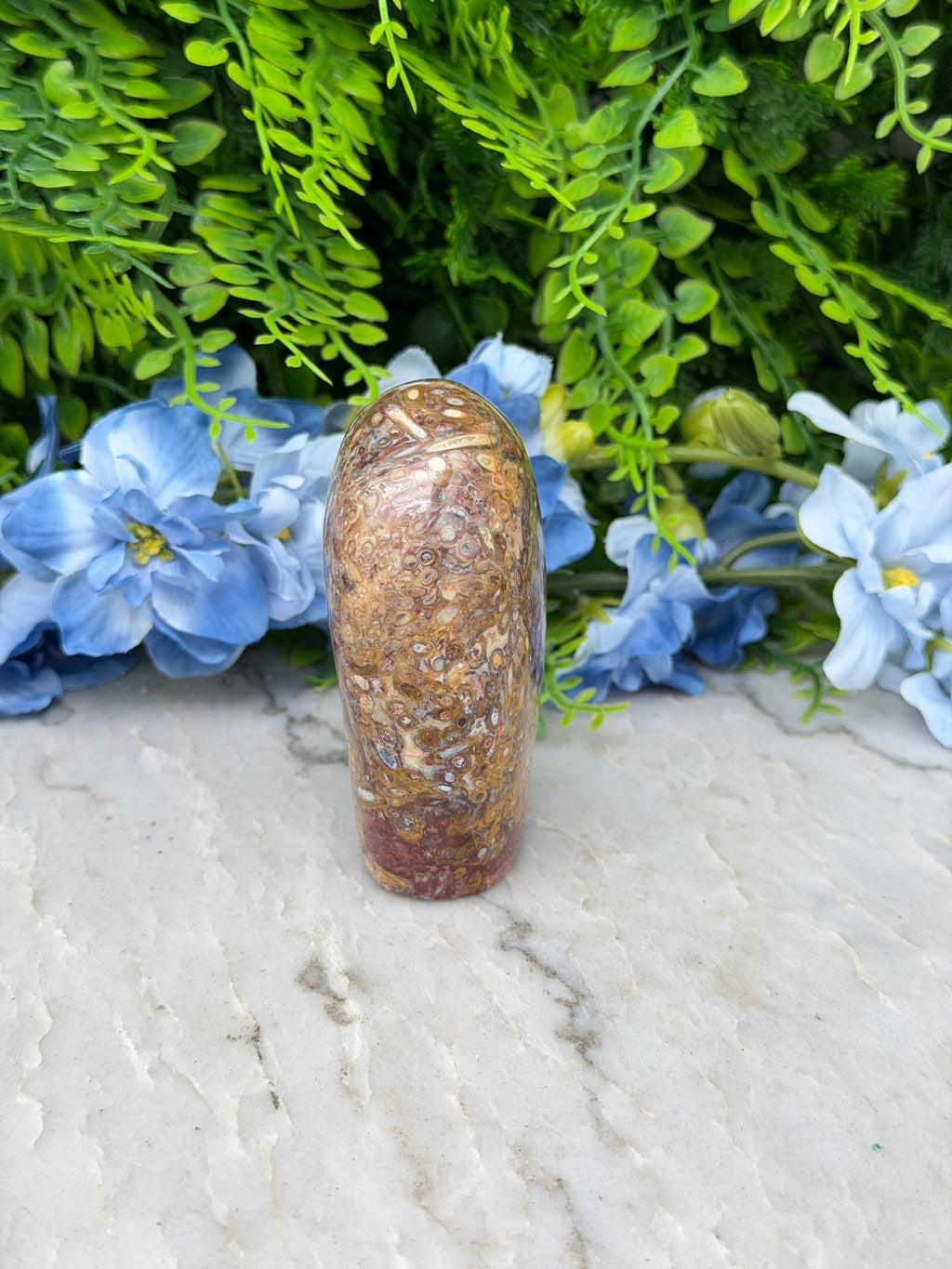 a stone or rock with a natural pattern, placed on a white surface next to a cluster of blue flowers.