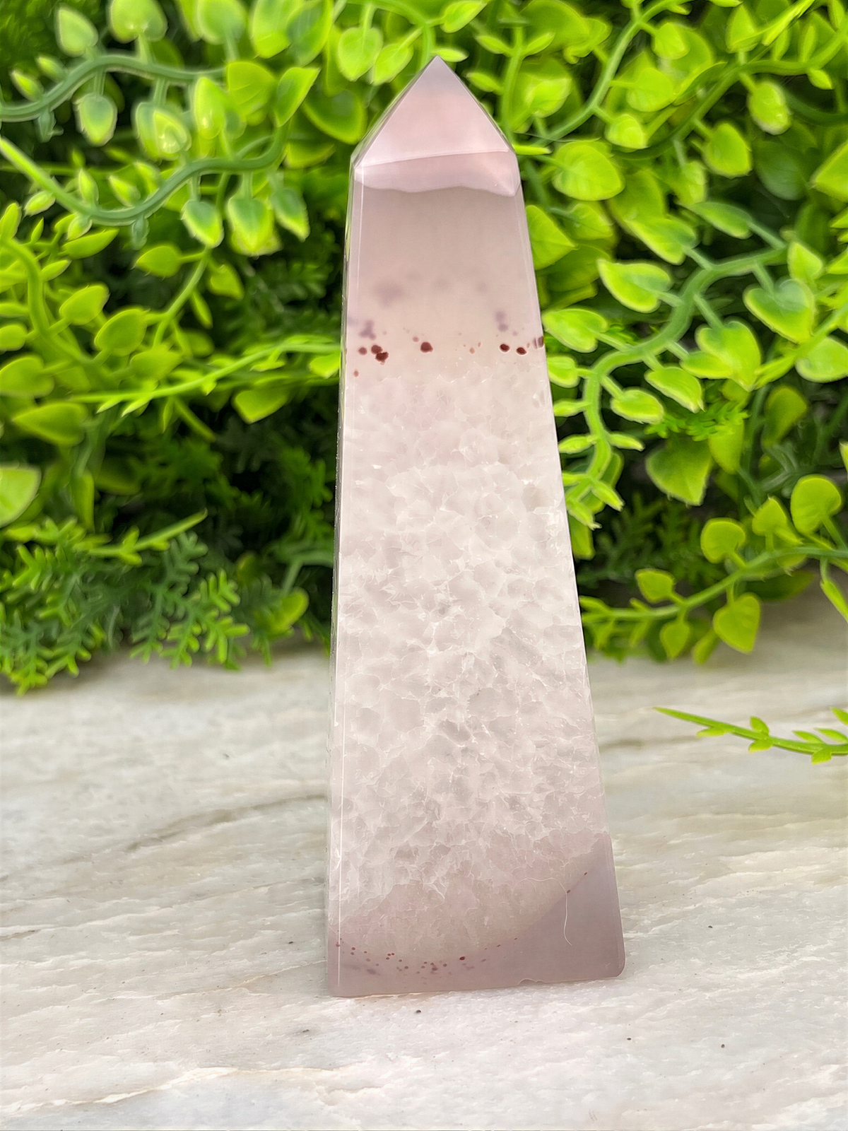 A pink jade crystal is displayed in the center of the image, surrounded by green foliage.
