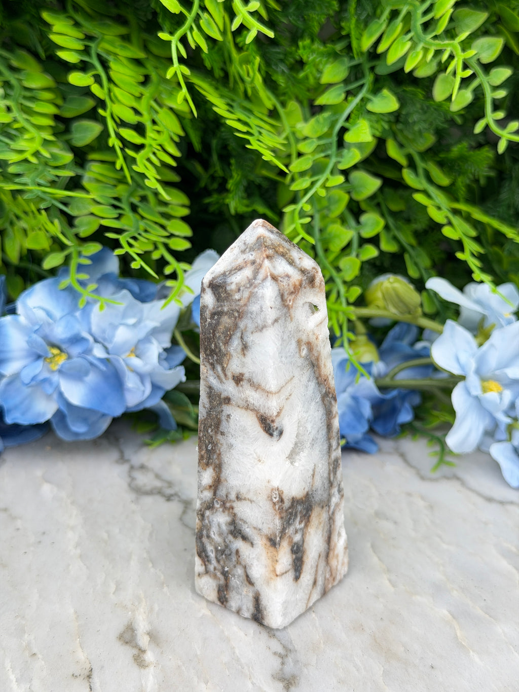 a marble-like stone or crystal surrounded by lush green foliage and blue flowers, creating a visually appealing and harmonious composition.
