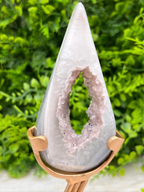 A white, triangular-shaped rock with a large, jagged opening in the center, displayed on a gold stand against a blurred green background.