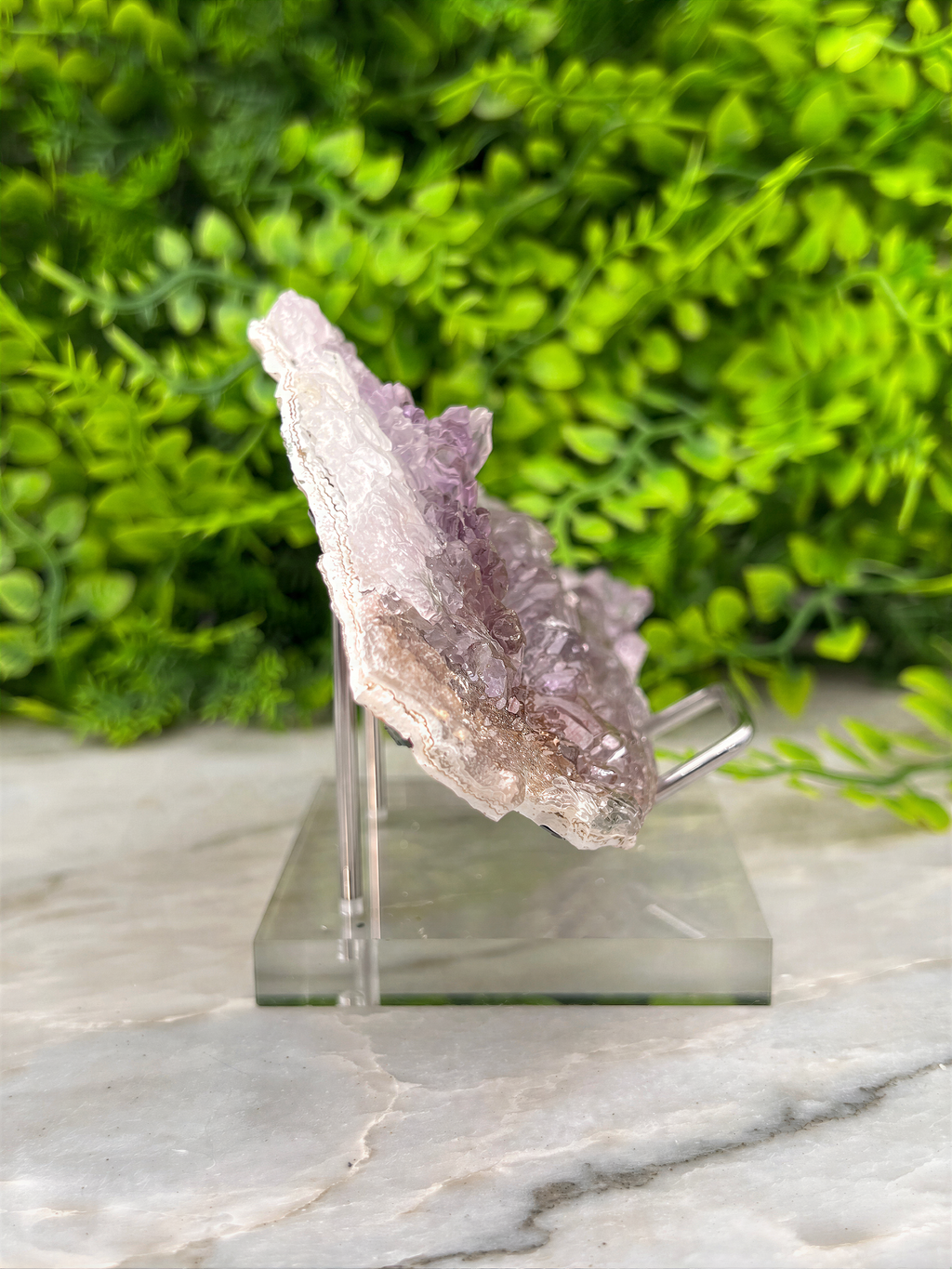 A piece of amethyst crystal is displayed on a clear stand, surrounded by a blurred green background.