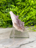 A piece of amethyst crystal is displayed on a clear stand, surrounded by a blurred green background.