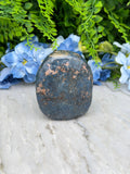 a close-up of a dark blue stone with some light spots, surrounded by vibrant blue flowers.