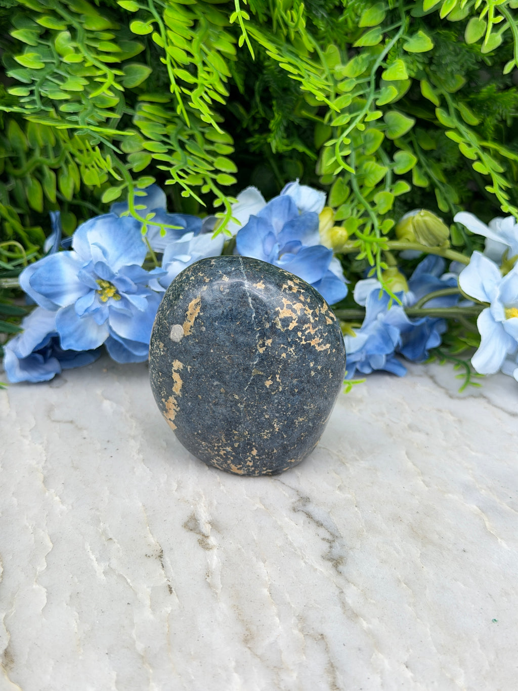 A black rock rests on a white surface, surrounded by vibrant blue flowers.