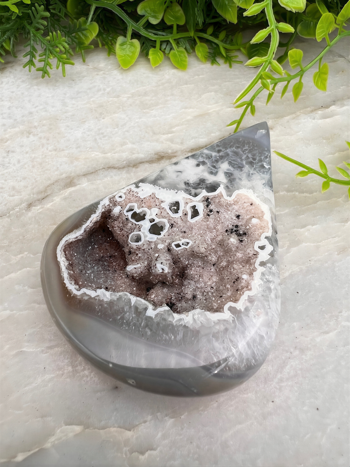A close-up image of a rock with a unique, irregular shape, surrounded by greenery.