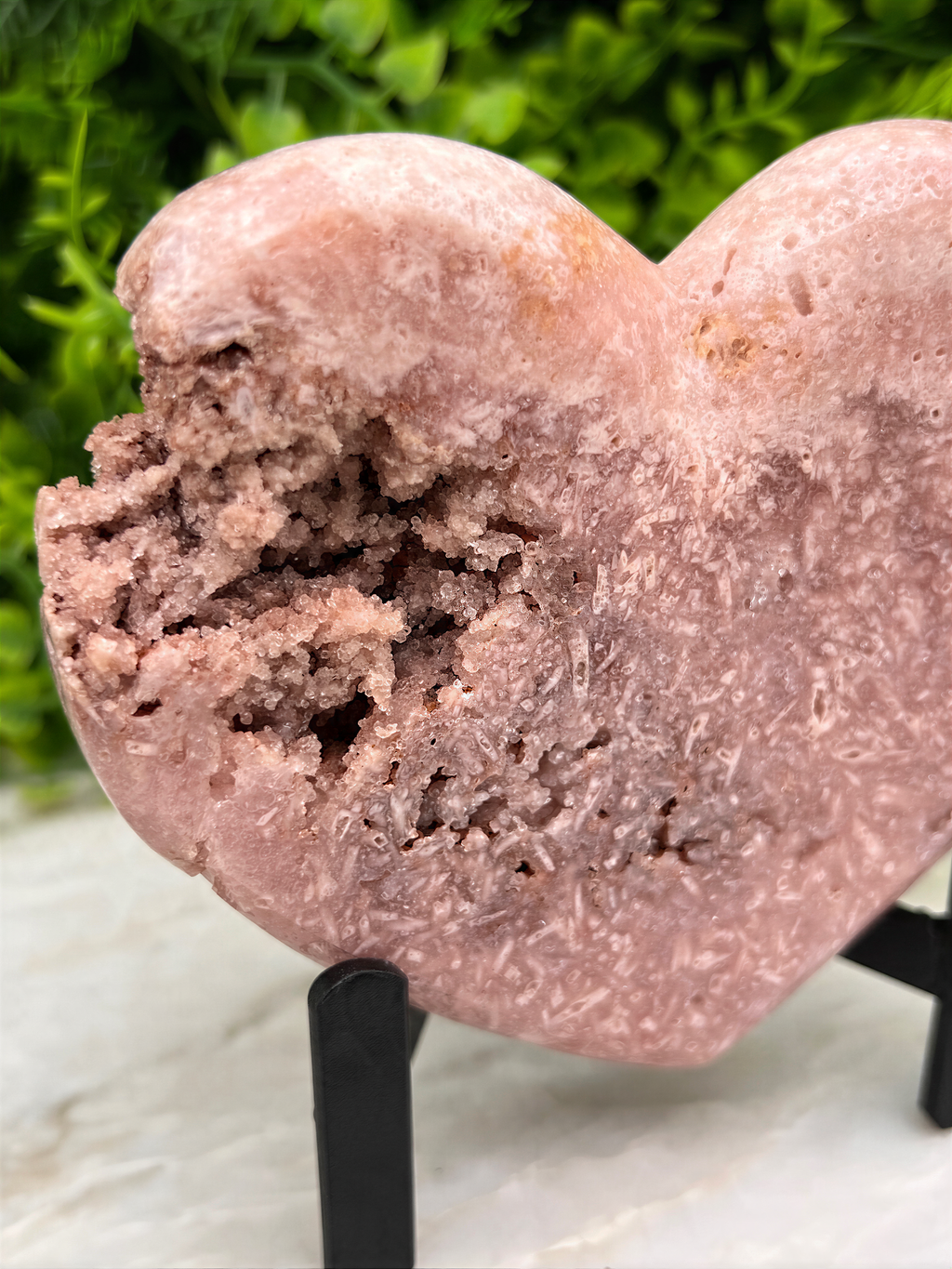 A pink heart-shaped crystal on display, with a blurred green background.