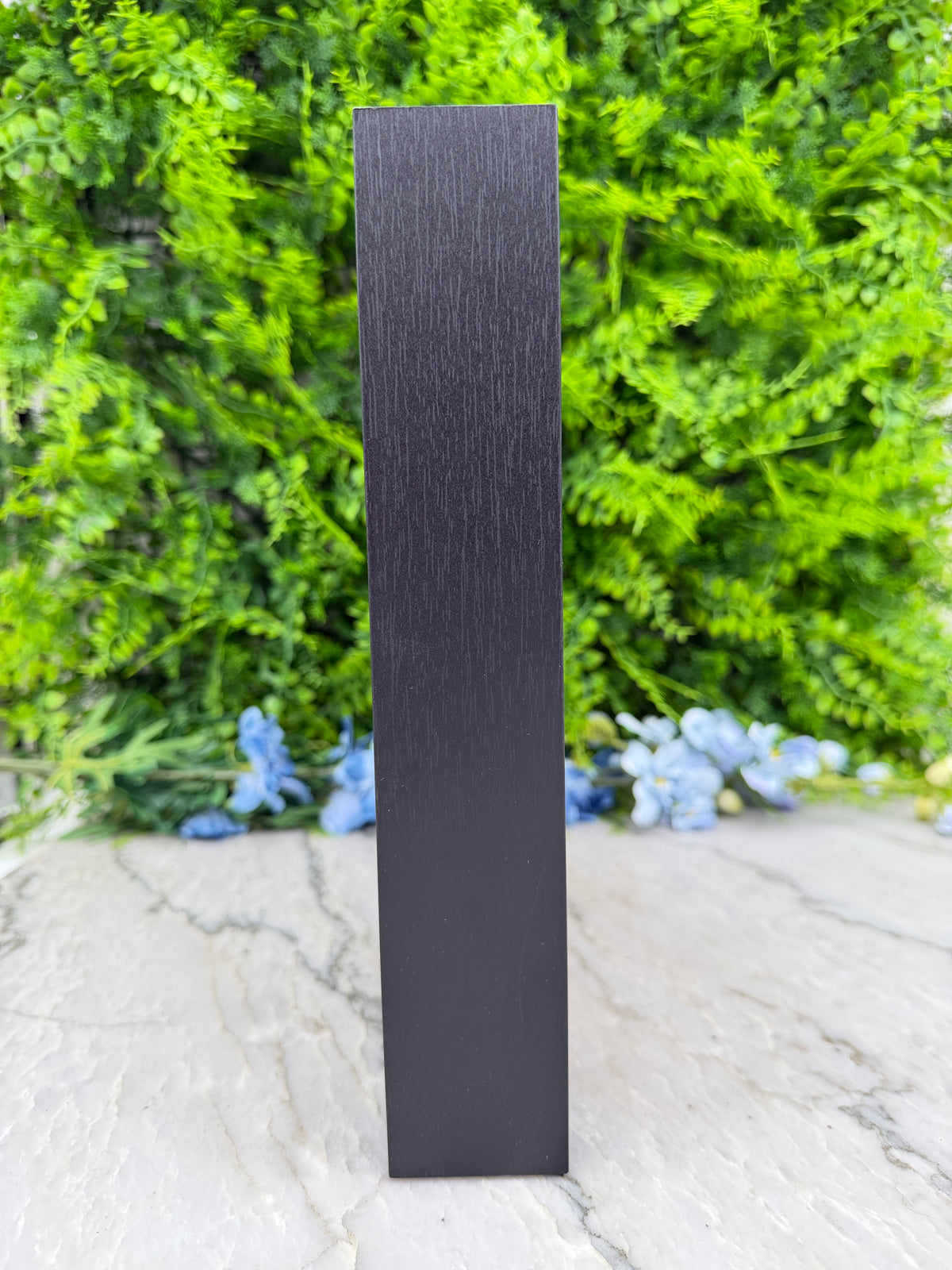 a black rectangular object placed against a backdrop of lush green foliage and delicate blue flowers.