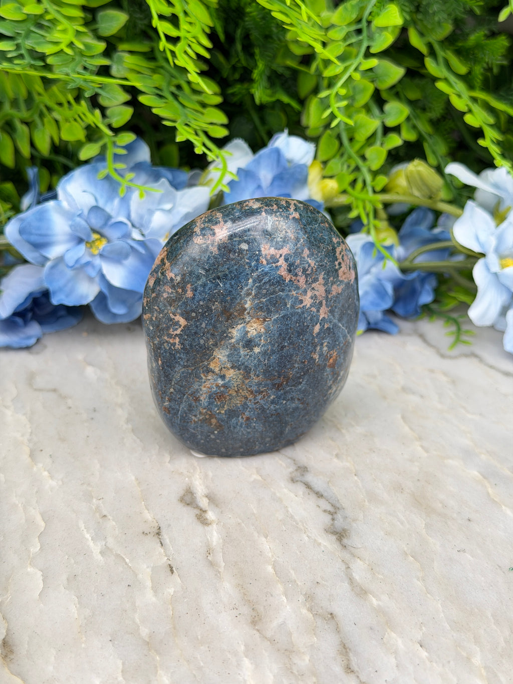 A dark blue rock rests on a white surface, surrounded by vibrant blue flowers.