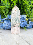 A white and green crystal sits on a marble surface, surrounded by blue flowers.