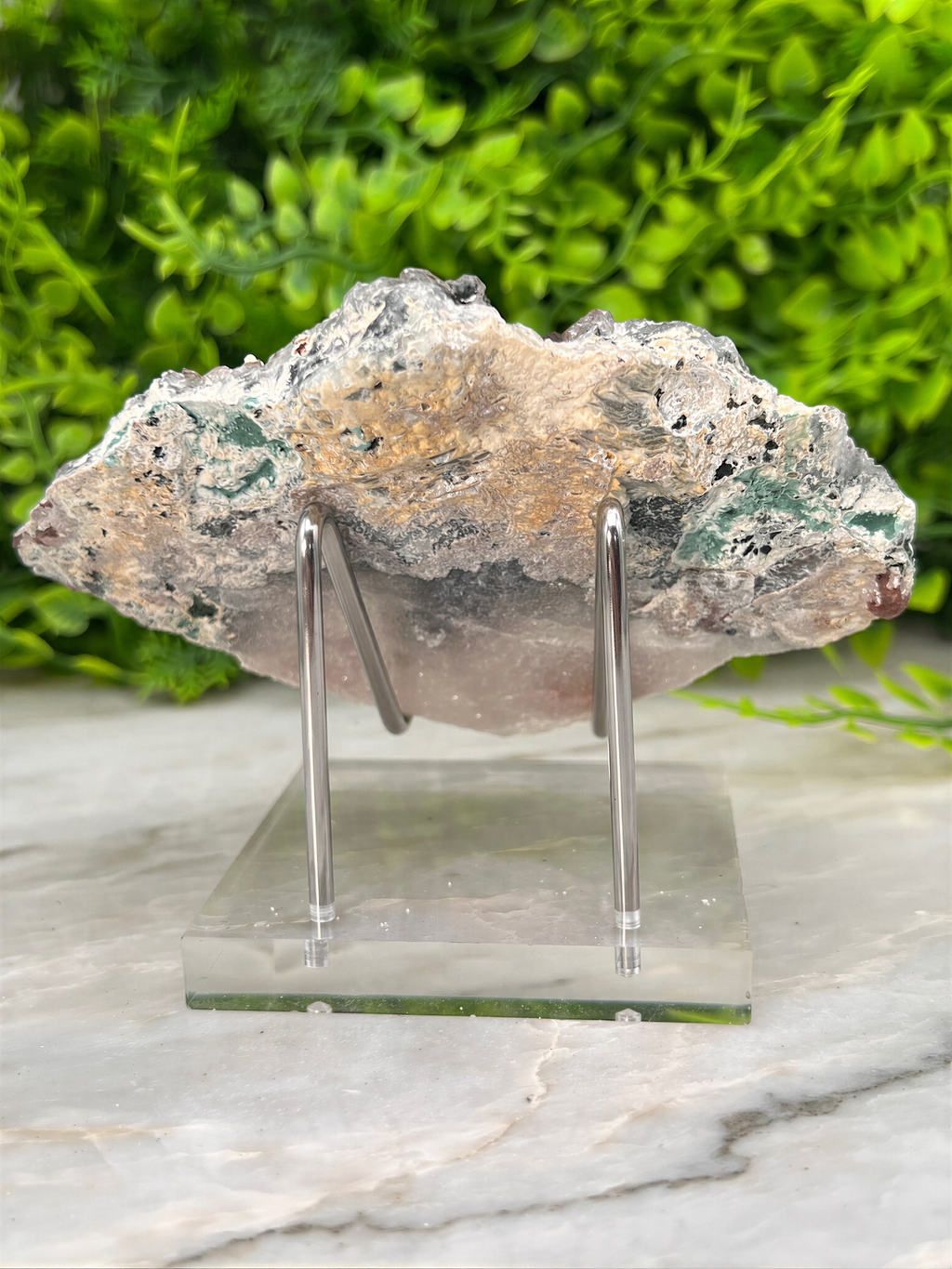 A piece of rock or mineral displayed on a clear stand, with a blurred green background.