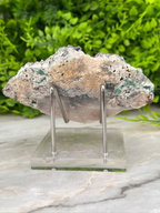A piece of rock or mineral displayed on a clear stand, with a blurred green background.