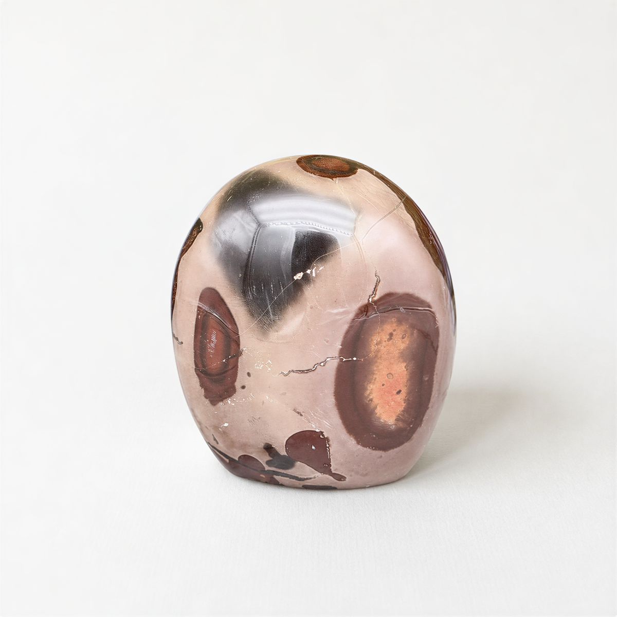 a round, textured stone or gemstone with a pattern of brown and orange spots, sitting on a white surface.