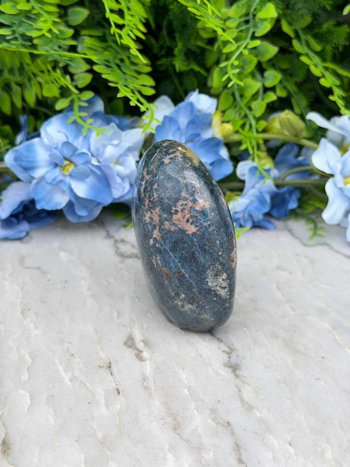 a close-up view of a dark blue rock resting on a white surface, surrounded by vibrant blue flowers.