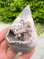 A hand is holding a piece of a geode with a unique, irregular shape and a white, speckled surface.