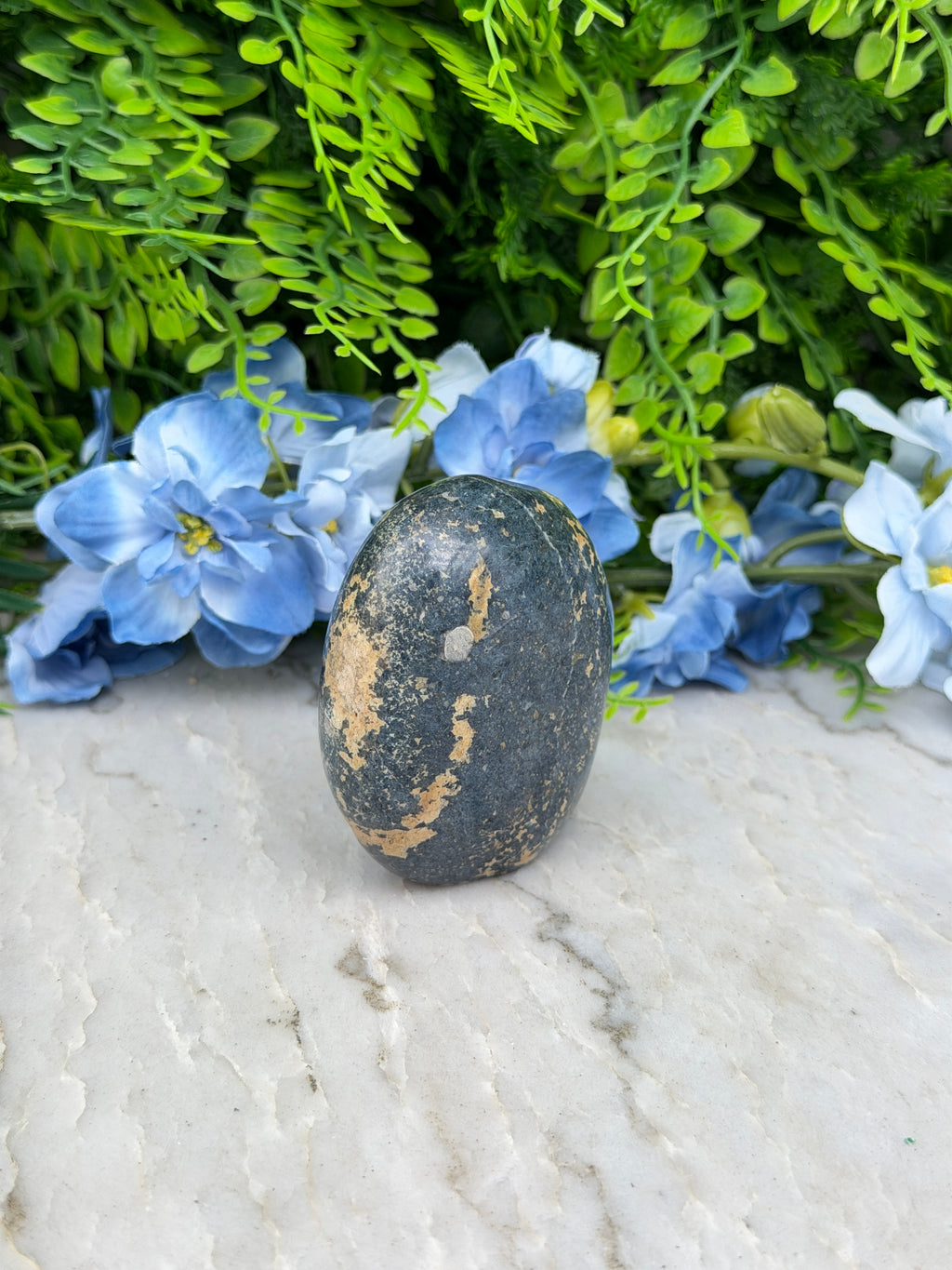 A black rock rests on a white surface, surrounded by vibrant blue flowers.
