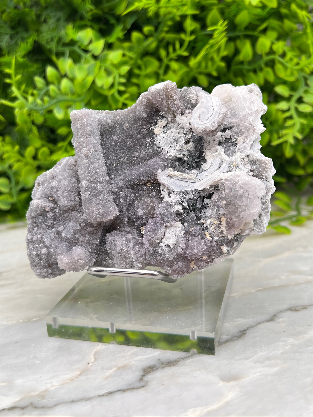 a large, irregularly shaped crystal or rock formation, possibly a type of quartz or amethyst, displayed on a clear glass stand.