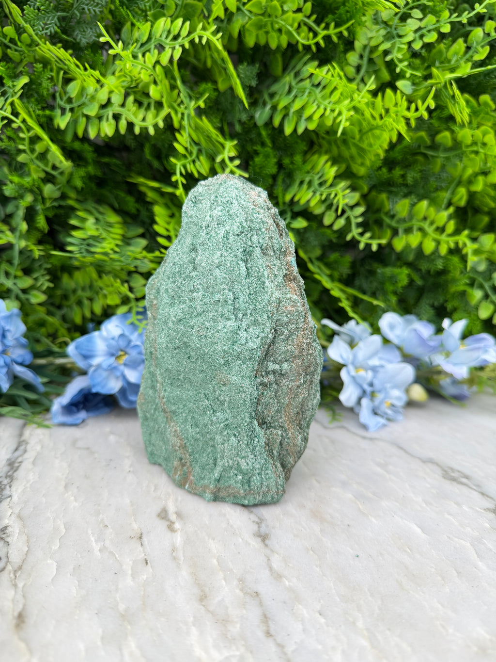 a large, green rock surrounded by lush green foliage and delicate blue flowers.