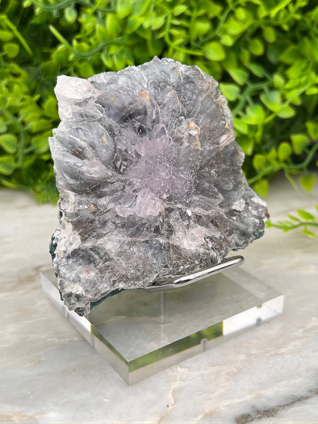 a large, irregularly shaped piece of gray rock with a purple hue, placed on a clear glass stand.