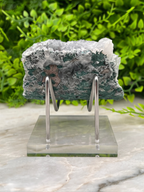 a piece of green and white rock, possibly a mineral, displayed on a clear stand.