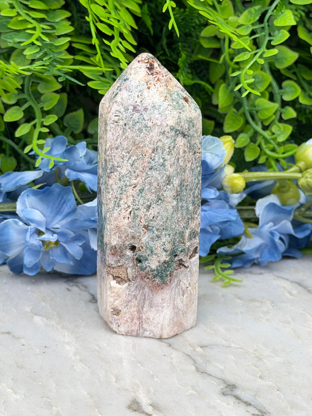 a stone jade crystal surrounded by lush green foliage and vibrant blue flowers.