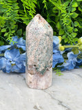 a stone jade crystal surrounded by lush green foliage and vibrant blue flowers.