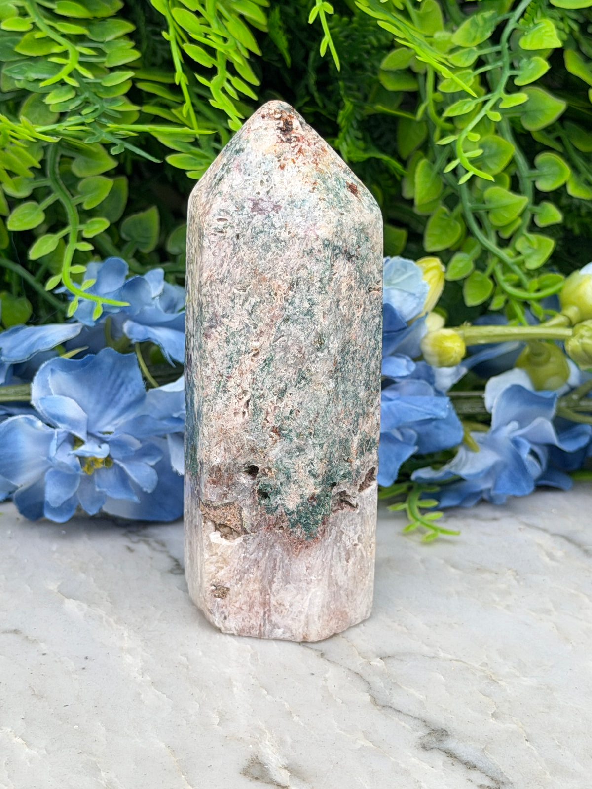 a stone jade crystal surrounded by lush green foliage and vibrant blue flowers.