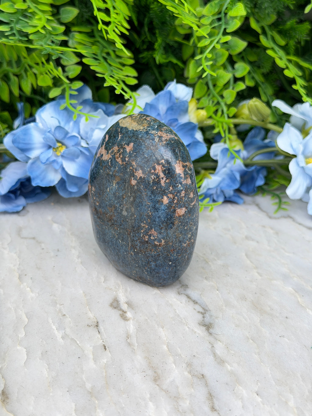 A dark blue rock rests on a white surface, surrounded by vibrant blue flowers.