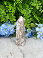 a close-up view of a stone or crystal with a natural, organic texture, surrounded by lush green foliage and delicate blue flowers.